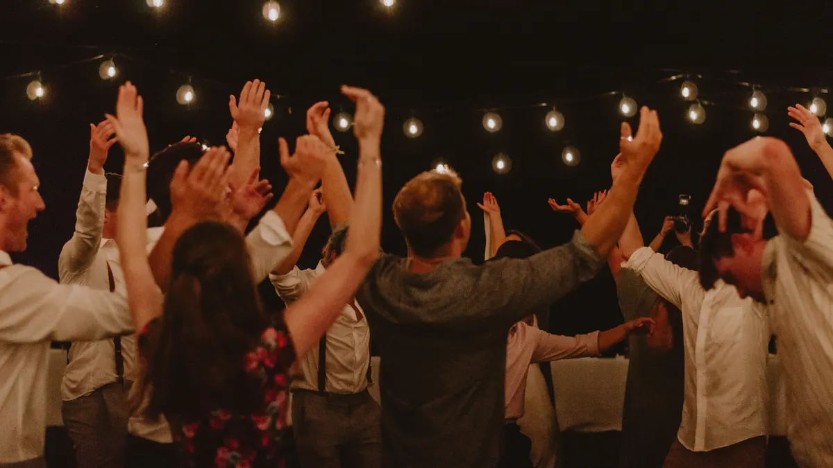 Group of adults dancing energetically under string lights at night.
