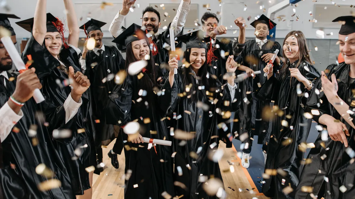A diverse group of graduates celebrating with confetti indoors, capturing achievement and joy.