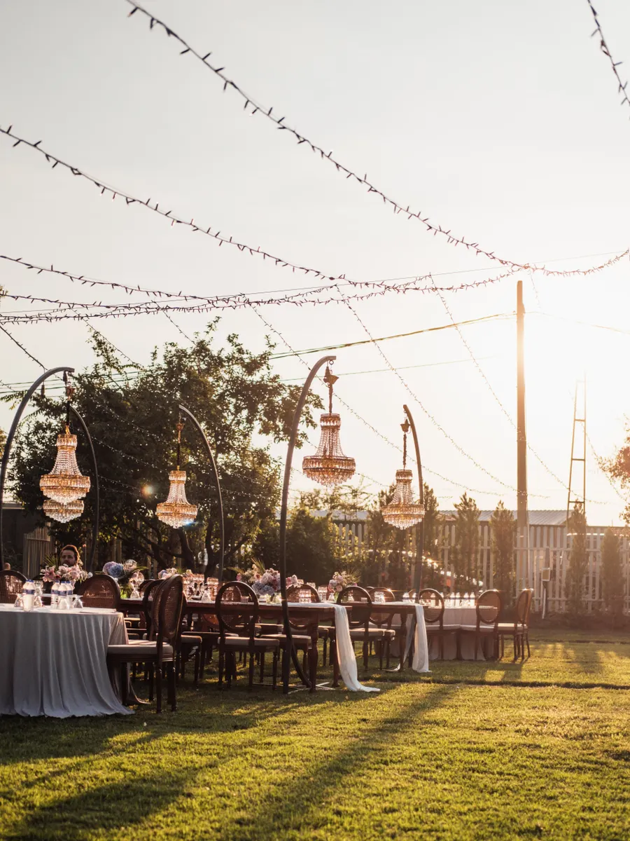 A beautifully decorated outdoor wedding venue with chandeliers and tables set for guests, bathed in golden sunset light.