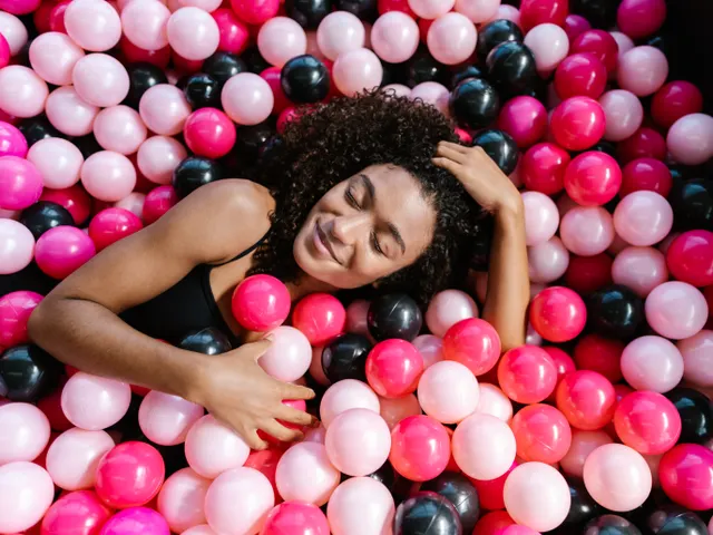 A joyful woman relaxing in a vibrant ball pit filled with pink and black plastic balls.